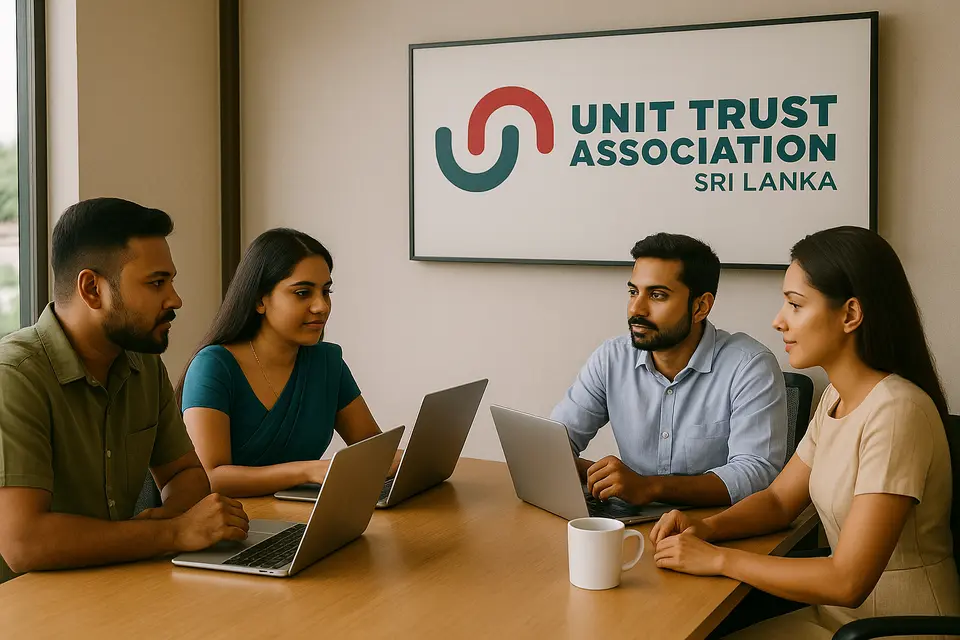 Four professionals sitting around a conference table with laptops, meeting under a sign for the Unit Trust Association of Sri Lanka.
